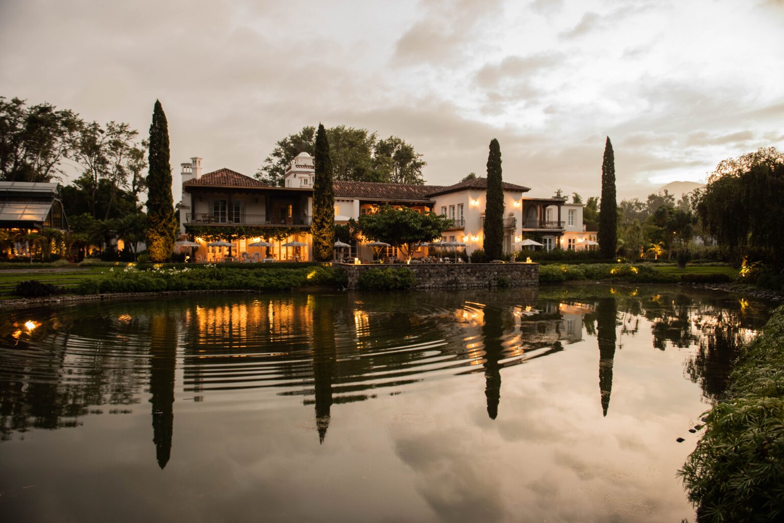 Vista al atardecer de Villa Bokéh, hotel guatemalteco distinguido por la Guía Michelin, con su fachada colonial reflejada en el lago